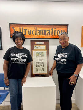 Two Black women pose by a plaque at the Safe House Museum.