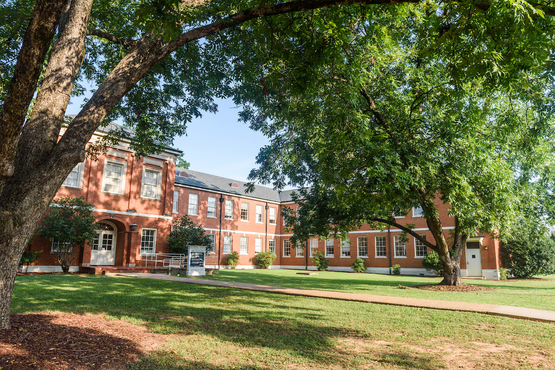 A red brick building sits in the background while several green trees are in the foreground on a sunny afternoon.
