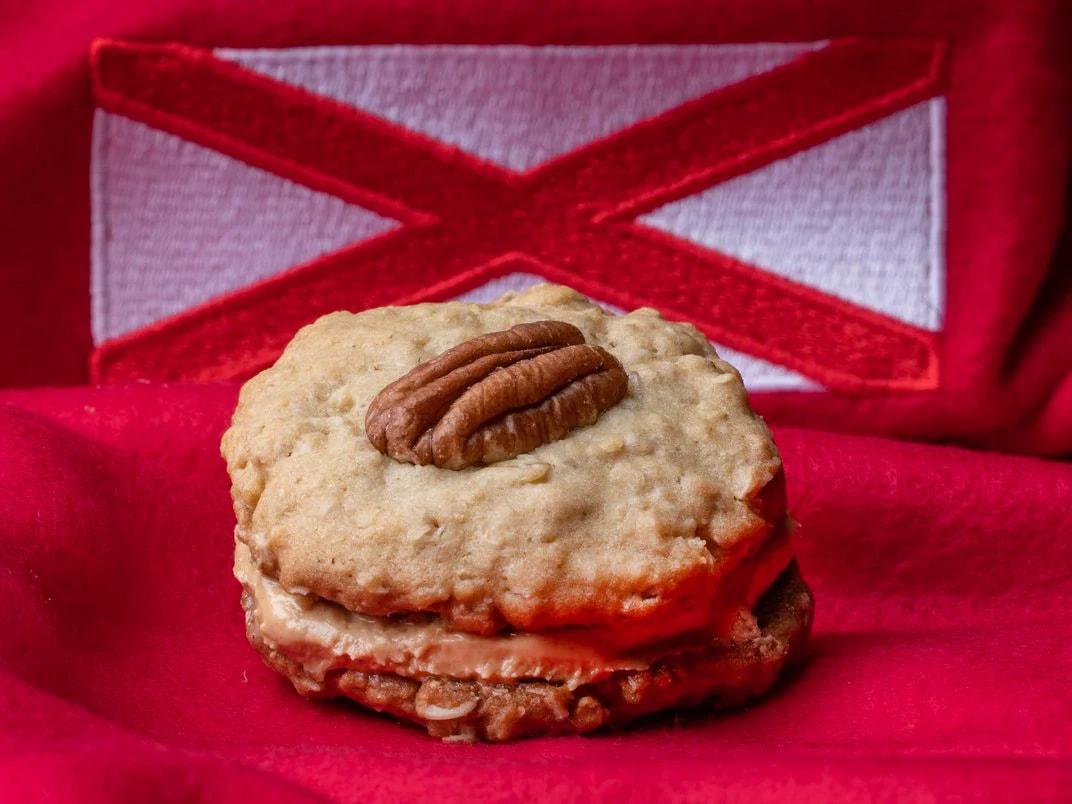 A cream-colored cookie with a light brown pecan sits on a red fabric background.